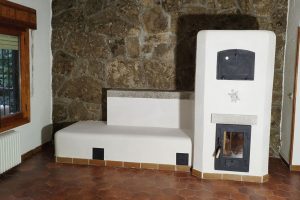 Ejemplo de estufa de inercia rocket con formas curvas y acabado en cal sobre fondo de pared de piedra