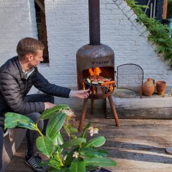 Foto de ambiente de la chimenea de exterior BonBono corten de Bonfeu encendida con parrilla.